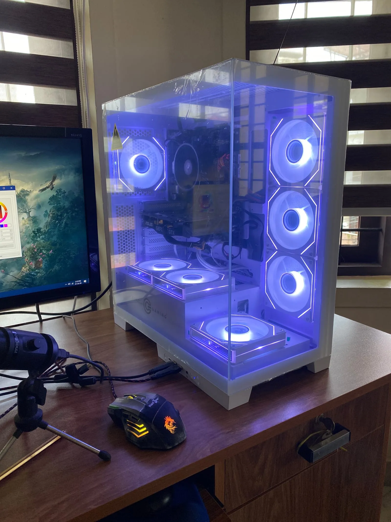 The finished build: a white Circle Defender ZX7 with panoramic glass, seven ARGB fans all lit uniform blue, with OpenRGB open on the monitor beside it.